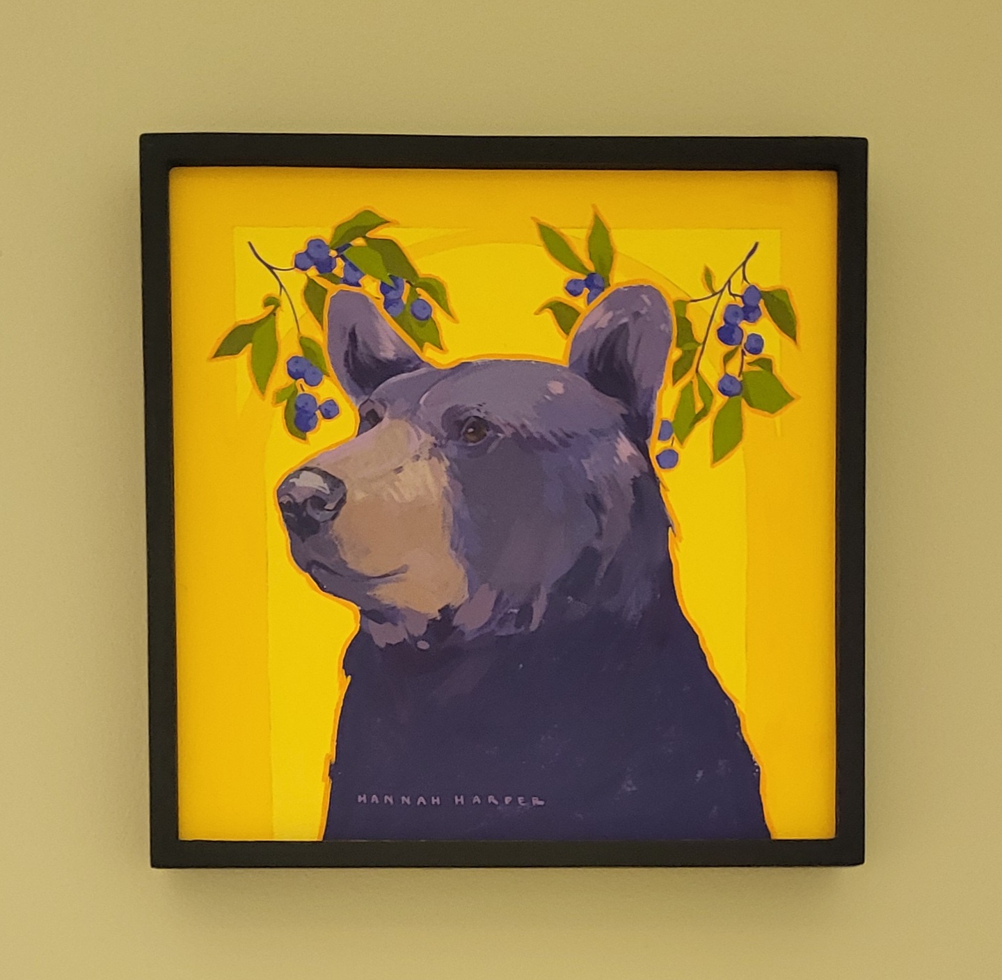 Painting of a bear on a bright yellow background with green leaves and blueberries in the backdrop.