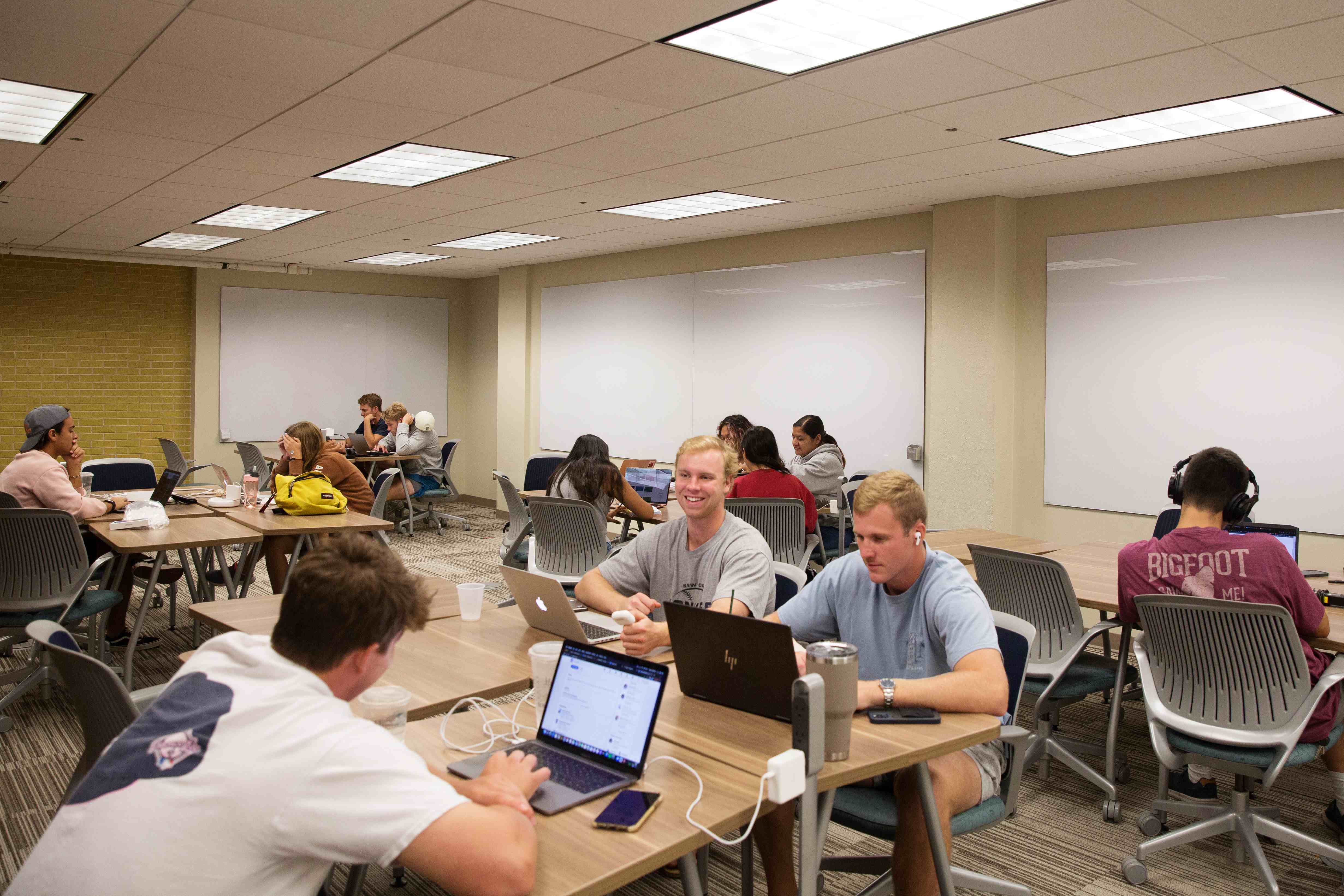 Classroom space with three whiteboards and multiple tables with chairs. 