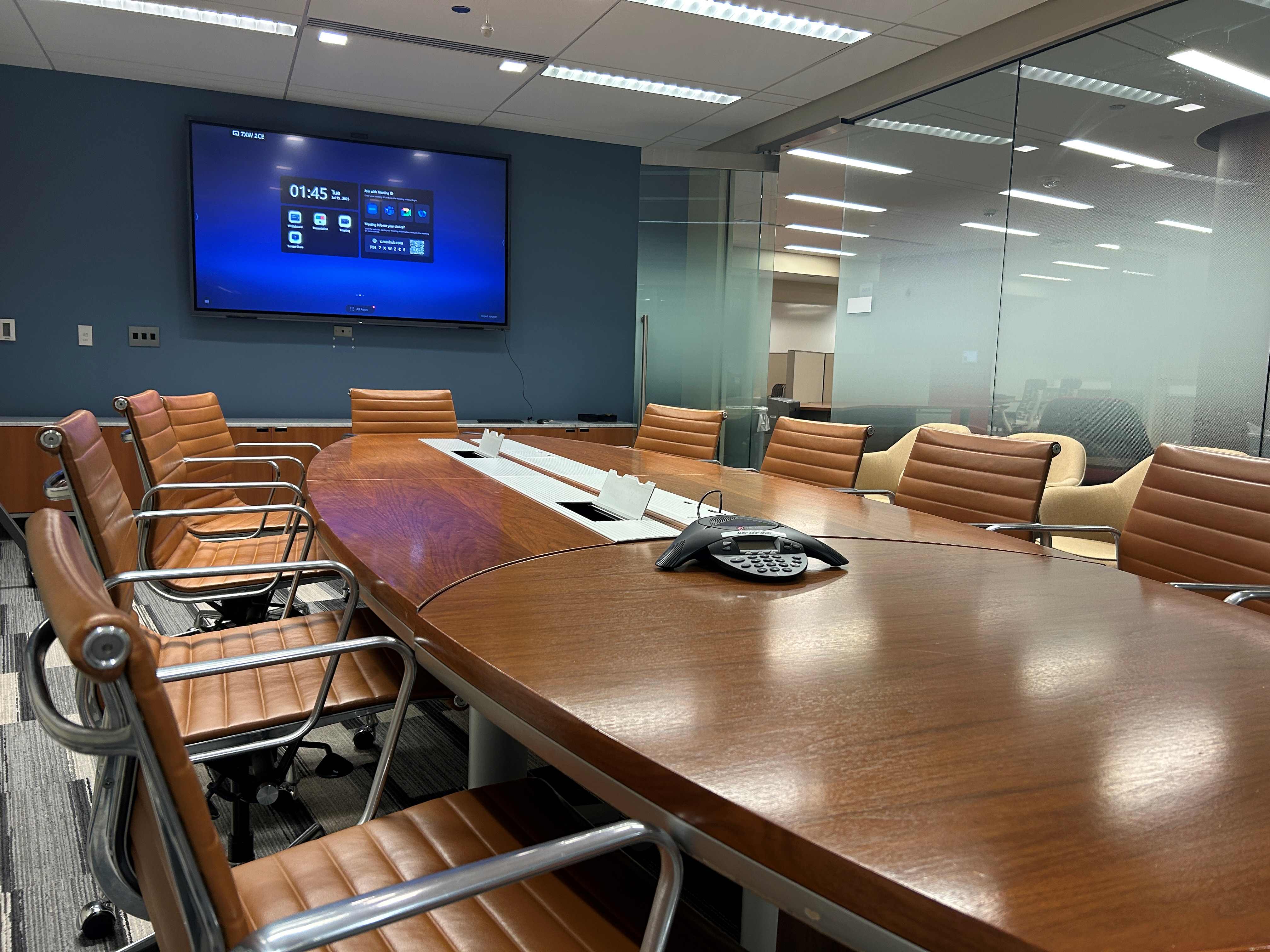 Large conference room with a conference table, several chairs, and a large display screen