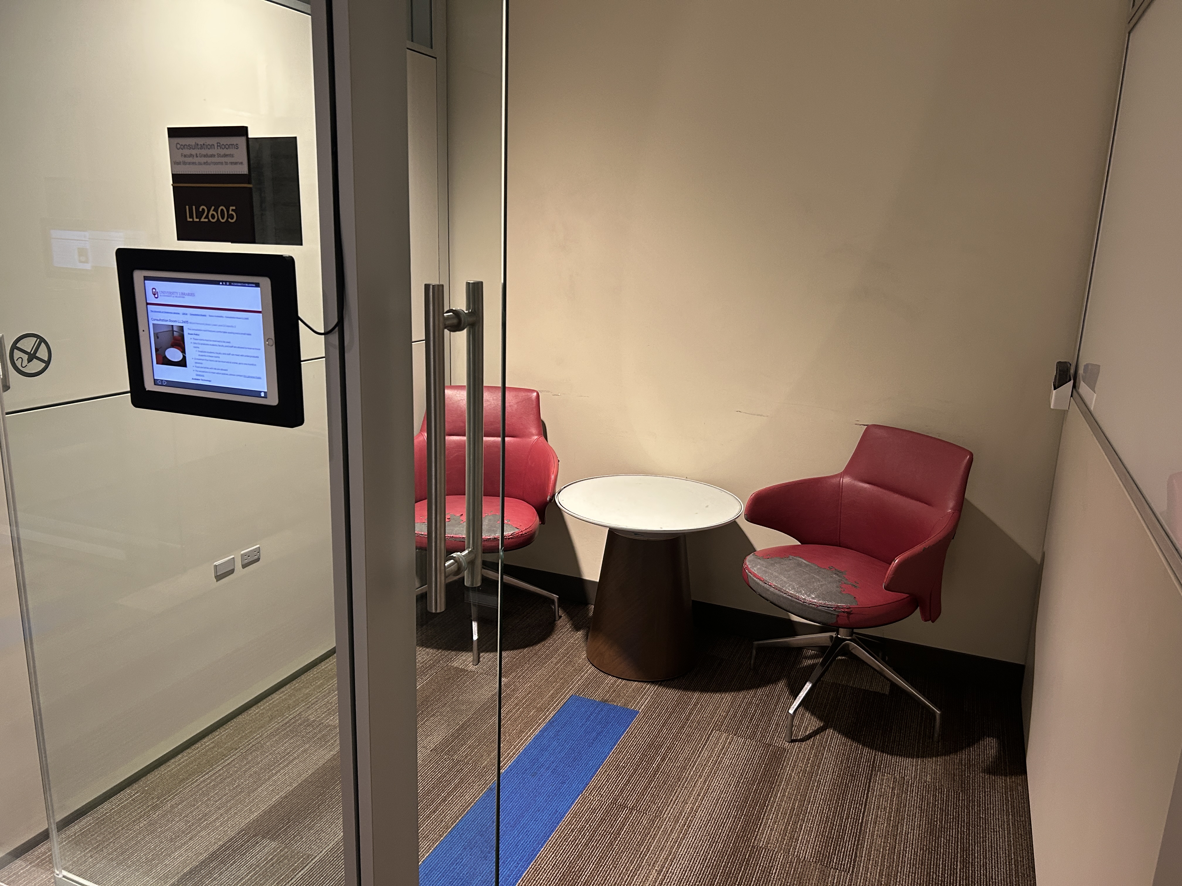 Small room with two red rolling chairs, a small table between them, and a whiteboard 