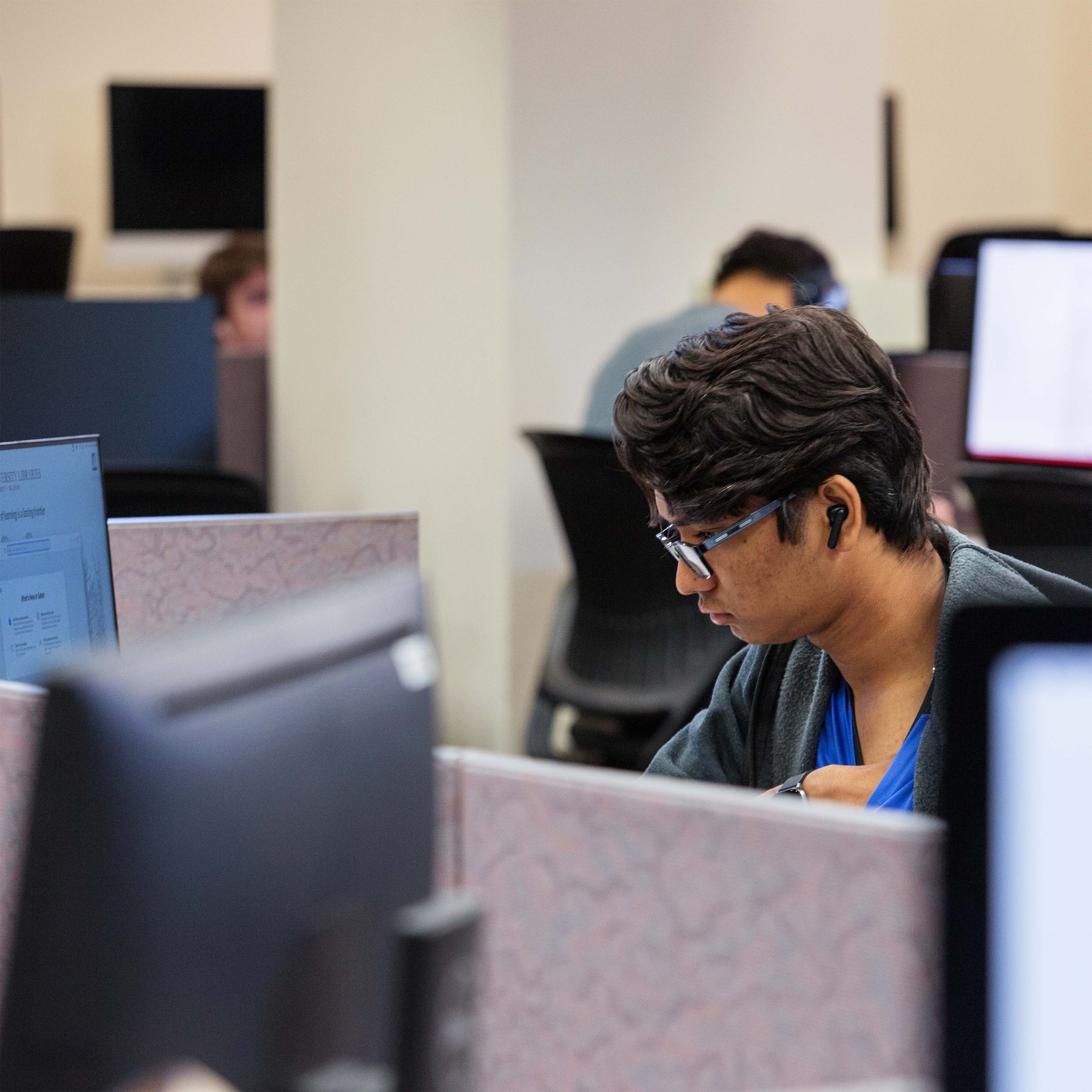 Male student sitting at a computer workstation in the computer lab concentrating while he looks at computer screen.