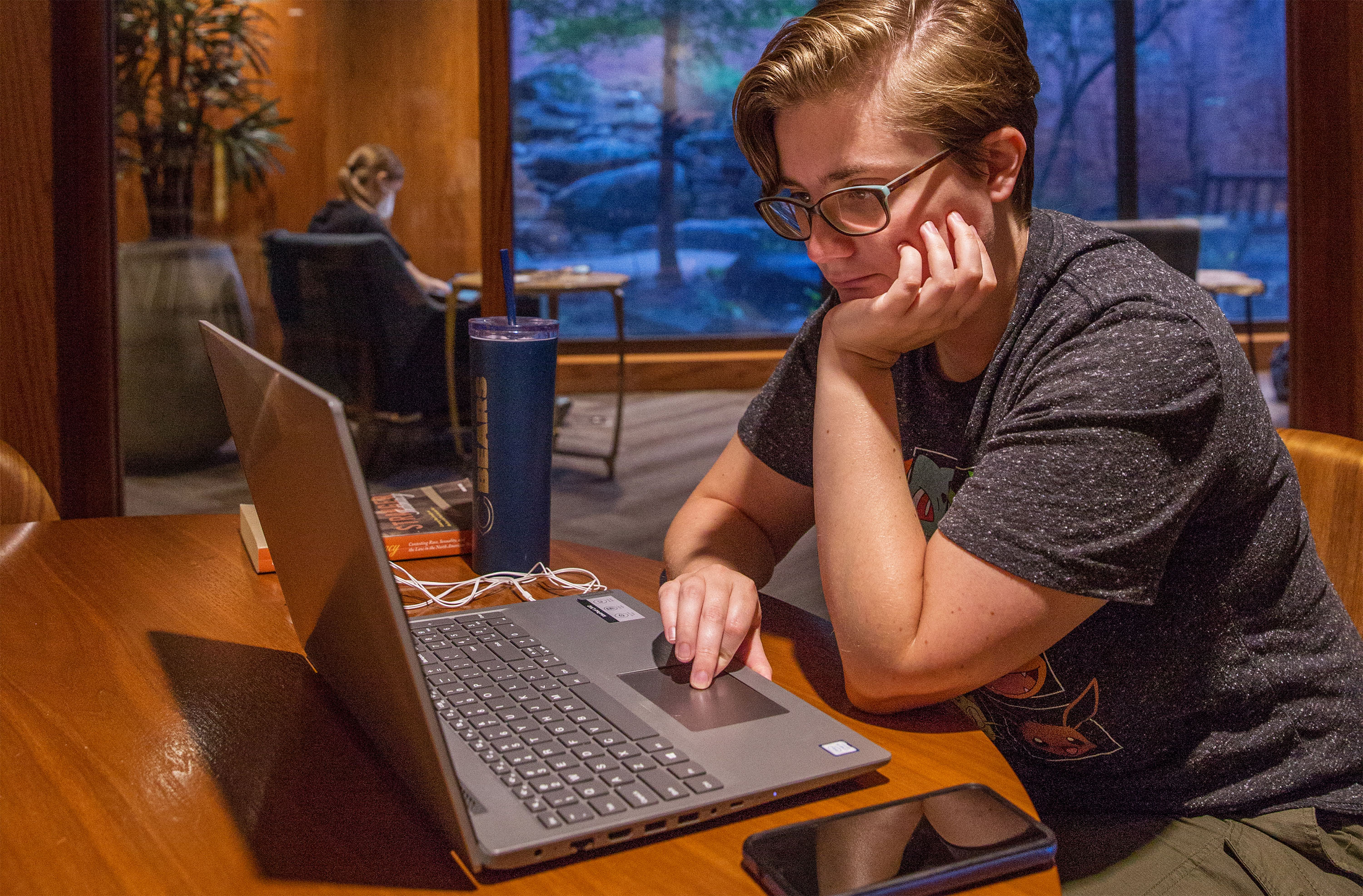 A student is in the Zarrow Center sitting at a round table working on a laptop and focusing on the screen.