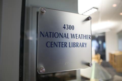 Closeup of sign on a glass door that reads "4300 National Weather Center Library."