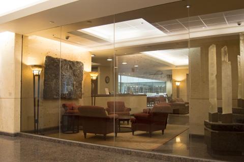 A modern lobby with glass walls showing plush armchairs around a small table on a carpet. Soft lighting creates a welcoming atmosphere.