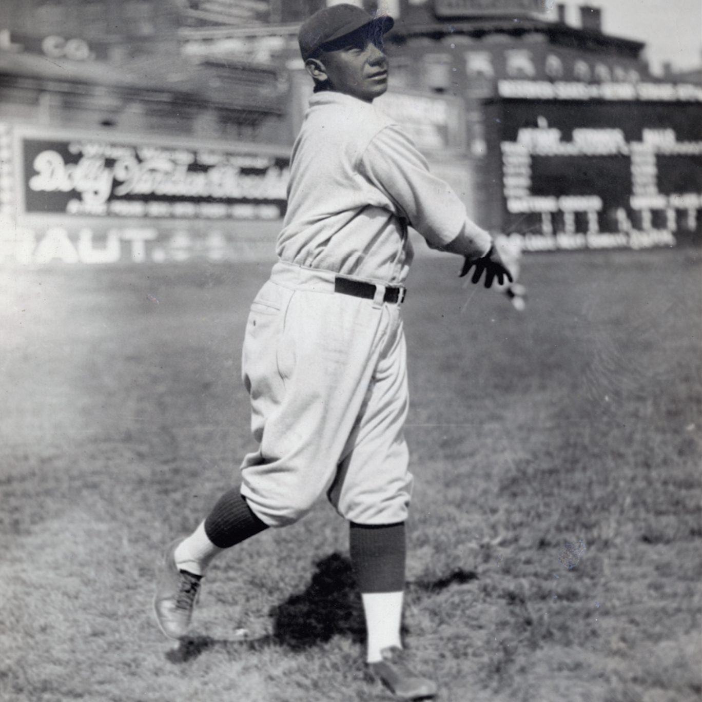 1922 vintage black-and-white photo of baseball player Mose Yellowhorse. He is mid-throw on a grassy field, wearing his Pittsburgh Pirate uniform and cap, with a stadium in the backdrop.